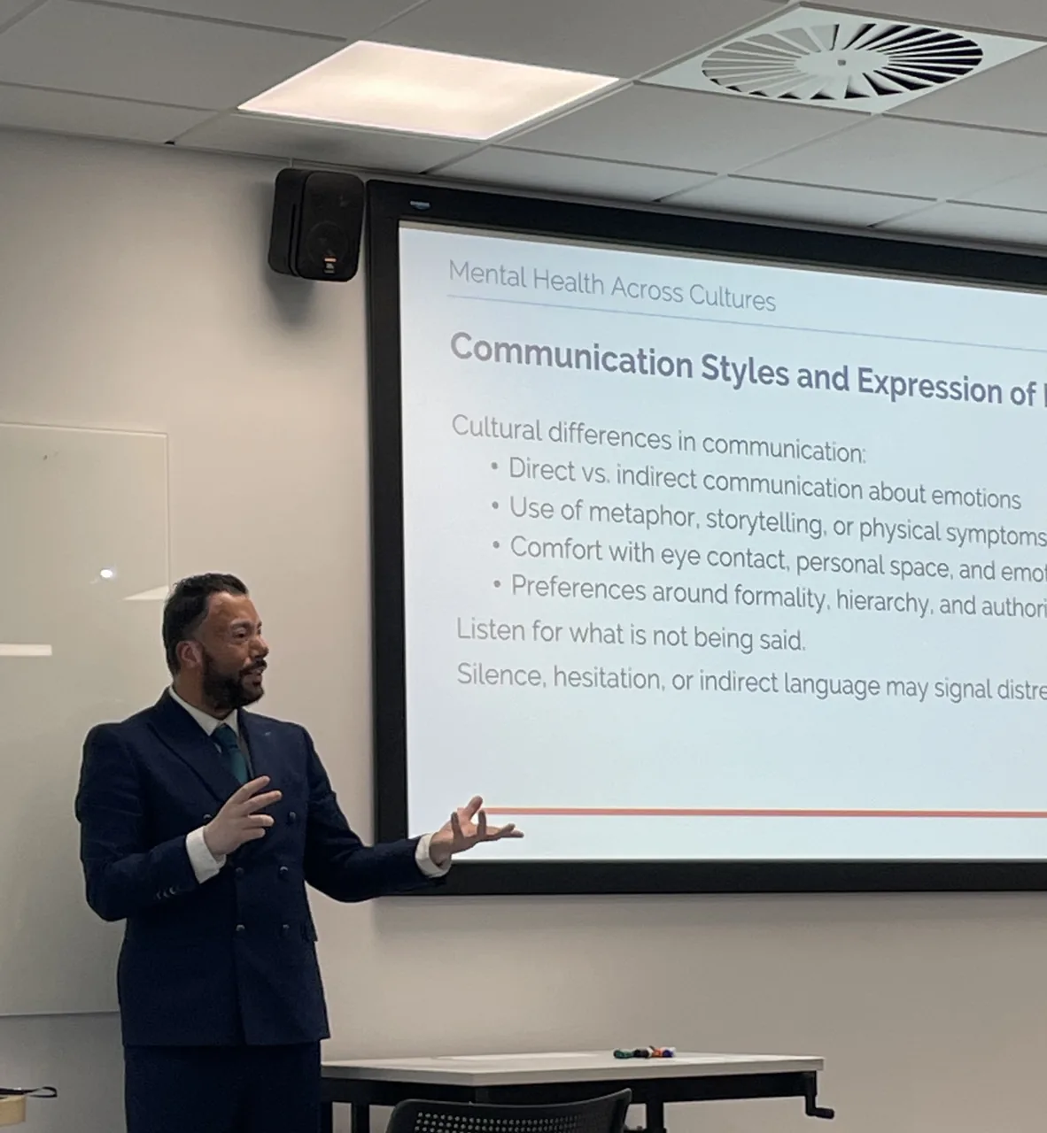 Raza Rahman delivering a Mental Health Across Cultures session beside a presentation slide